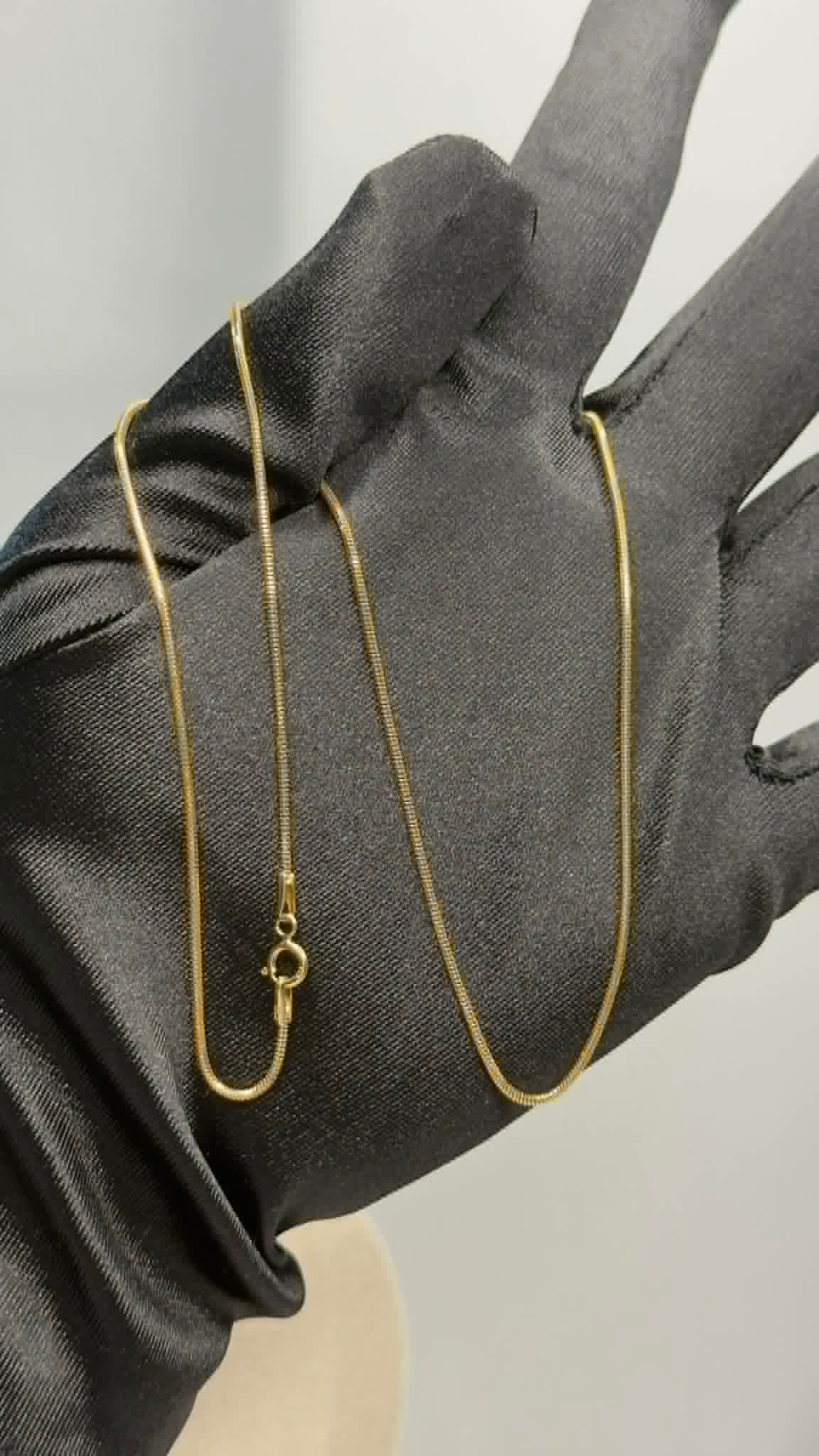 Fine gold snake chain held on a gloved hand